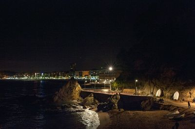 Illuminated city by sea against sky at night