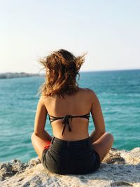 Rear view of woman sitting at beach against sky