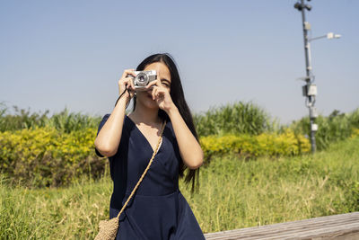 Woman photographing with camera on land against clear sky