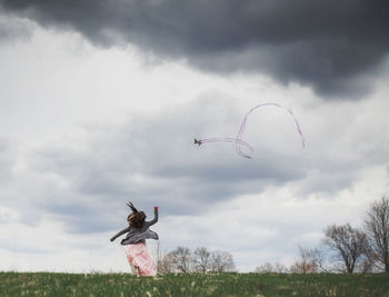 Rear view of playful girl flying kite against cloudy sky at park