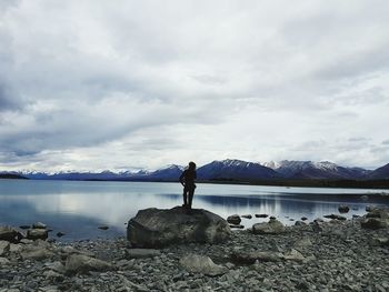 Rear view of person standing on rock by lake against sky