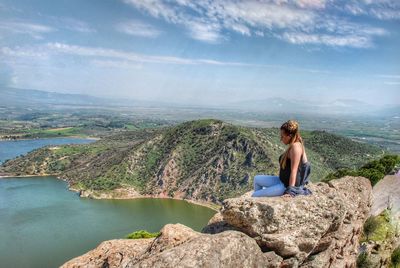 Woman sitting on rock looking at mountain against sky