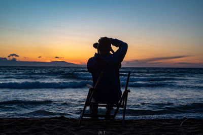 Rear view of person photographing sea during sunset