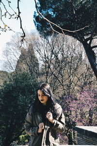 Young woman standing by tree against plants