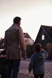 Rear view of son pointing while standing by father on footpath during sunset