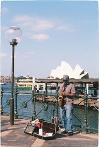 Man standing by railing against sky