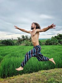 Shirtless man running on field against sky