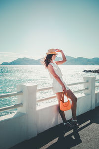 Side view of woman drinking water while sitting at beach against sky