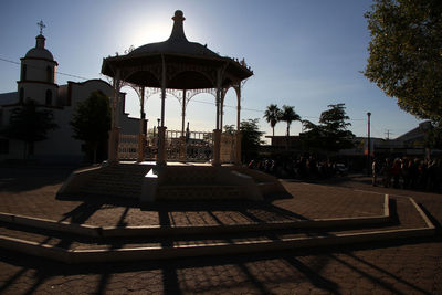 Gazebo by swimming pool in city against sky during sunset