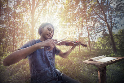 Portrait of smiling young woman sitting on tree trunk in forest