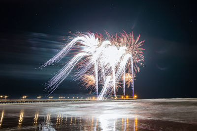 Firework display over pier by sea against sky at night