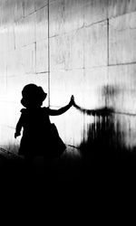 Rear view of silhouette girl standing by wall