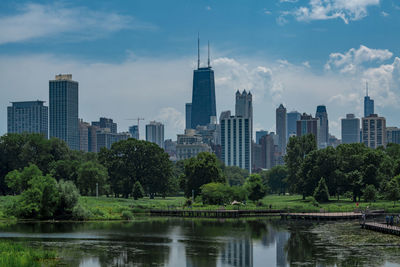 Lake by modern buildings in city against sky