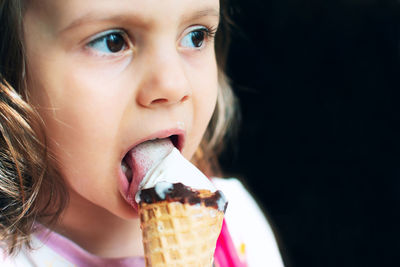 Close-up of girl eating icecream against black background