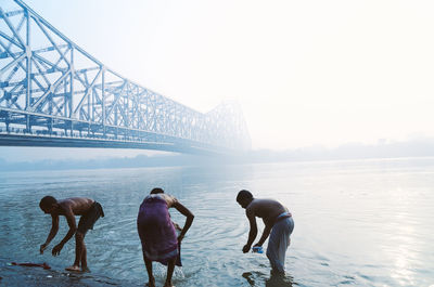 Men washing clothes at seashore during foggy weather
