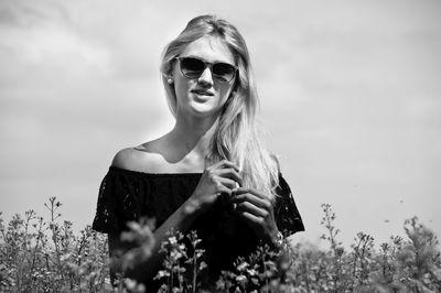 Portrait of young woman wearing sunglasses on field against sky