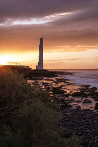 Lighthouse by sea against sky during sunset