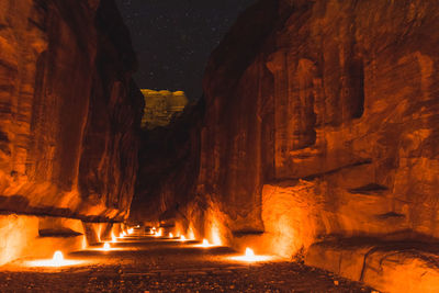 Illuminated walkway amidst rock formations at petra at night