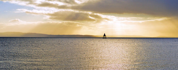 Silhouette person in sea against sky during sunset