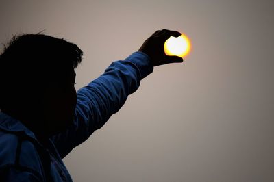 Low angle view of hand holding sun during sunset