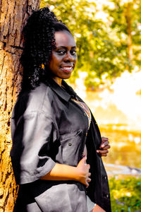 Portrait of smiling young woman standing against tree trunk