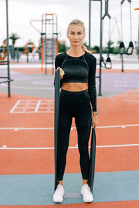 Young athletic woman is training on the sports ground using sports elastic bands.