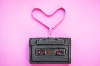 Close-up of gray audio cassette with heart shape against pink background