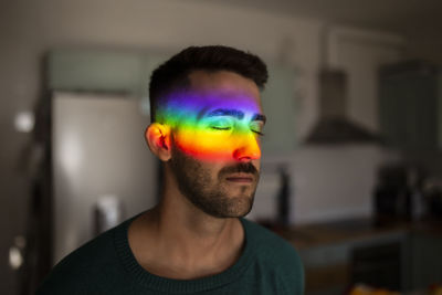 Rainbow light hitting face of young man standing indoors with closed eyes