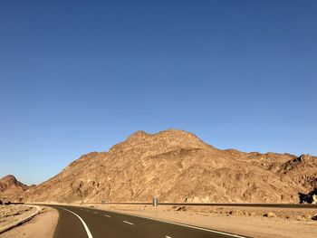 Road by desert against clear blue sky