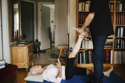 Midsection of male caregiver guiding senior woman while exercising at home