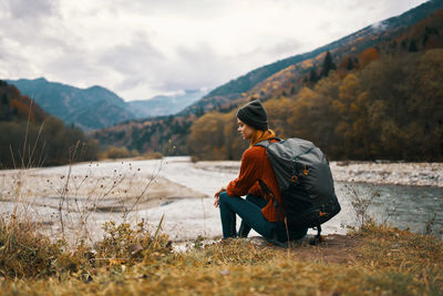 Full length of man sitting on mountain against sky