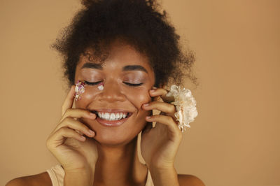 Smiling teenager girl applying petals on face against yellow background