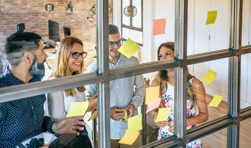 Happy business people in a work meeting standing placing sticky notes on a glass wall