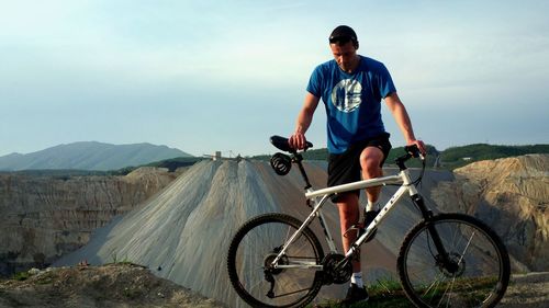 Man with bicycle on mountain against sky