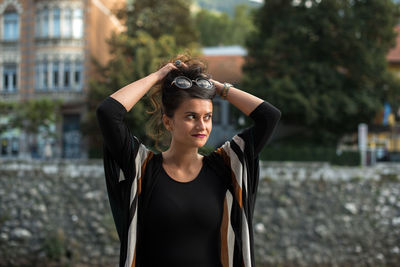 Young woman looking away while tying hair against buildings