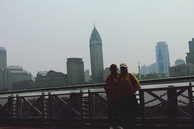 Man standing on bridge against buildings in city