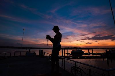 Silhouette man standing on pier by sea against sky during sunset