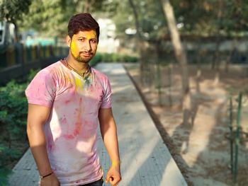 Portrait of young man smeared with multi colored powder standing on footpath
