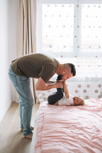 Happy father young man and baby girl little daughter having fun on bed in room at home