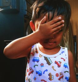 Close-up of baby boy covering face with hand while standing at home