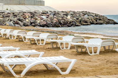 Empty chairs at beach against sky