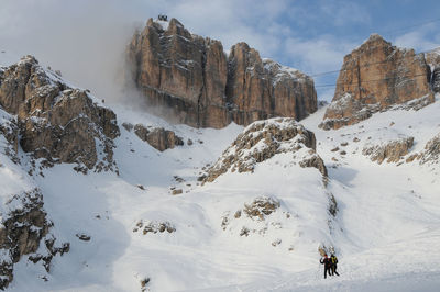 People climbing on snowcapped mountains against sky