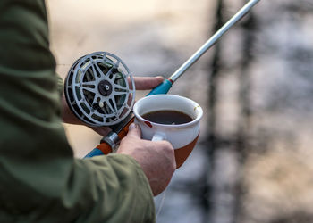 Close-up view with fisherman's hands, fishing reel and tea cup on a blurred background, fishing 