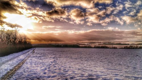 Snow covered landscape against sky during sunset