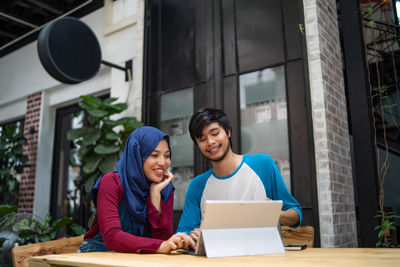 Low angle view of couple using digital tablet while sitting at sidewalk cafe