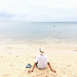 Rear view of man sitting on shore at beach against sky