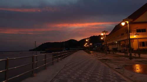 Street amidst illuminated city against sky at sunset