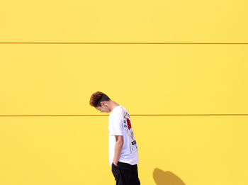 Side view of man standing against yellow background
