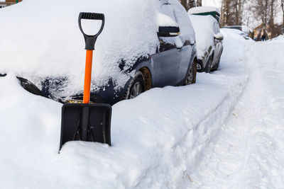 Plastic snow shovel in front of snow-covered car at winter morning