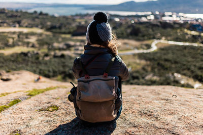 Rear view of woman sitting on rock looking at landscape